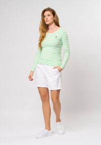 Groen en wit gestreept shirt met lange mouwen en een ronde halslijn, gecombineerd met witte shorts met zakken en omgeslagen zoom, gedragen met witte sneakers.