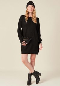 Svart stickad klänning med lång ärm, rund halsringning och avslappnad passform. Matchad med svarta ankelstövlar och en liten svart kuvertväska.
