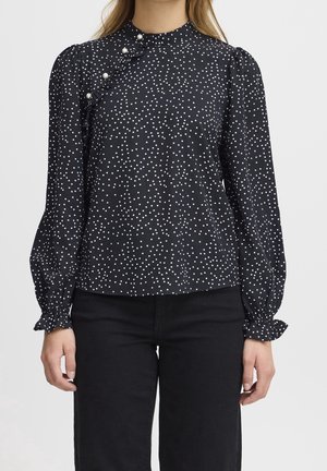 Blusa nera con pois bianchi, scollo alto, dettaglio arricciato con bottoni decorativi, maniche lunghe con polsini arricciati, tessuto morbido.