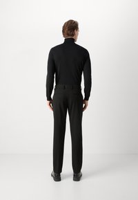 Col roulé noir, coupe slim, texture côtelée ; associé à un pantalon noir ajusté. Design simple sans logos ni motifs visibles, matériel minimal.