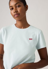 Ανοιχτό μπλε βαμβακερό μπλουζάκι με κοντά μανίκια, στρογγυλή λαιμόκοψη και κόκκινη ταμπέλα με το λογότυπο Levi's στο αριστερό στήθος. Λείο, καθημερινό σχέδιο.