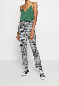 Camisole verte à encolure festonnée associée à un pantalon noir et blanc à motifs, portée avec des baskets montantes noires.