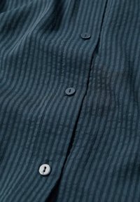 Gros plan sur un tissu bleu foncé avec des rayures verticales et trois boutons cousus le long d'une couture centrale.
