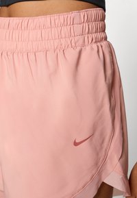 Pink sports shorts made of lightweight fabric, featuring an elastic waistband, side slit design, and a small red Nike logo on the side.