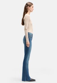 Dzwony z niebieskiego denimu z talią sięgającą do środka, pięciokieszeniowym krojem i subtelnym przetarciem. Połączone z czarnymi, spiczastymi butami.