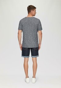 Szara, teksturowana koszulka, ciemne dżinsowe szorty z podwiniętymi nogawkami i białe sneakersy, widok z tyłu na jednolitym tle.