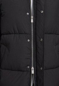 Čierna puffová bunda s prešívanou textúrou, s predným zipsom a patentkami, a so šedými kovovými detailmi.