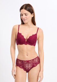 Set reggiseno e slip in pizzo bordeaux con motivi floreali, bordi smerlati e un piccolo fiocco decorativo sullo slip.