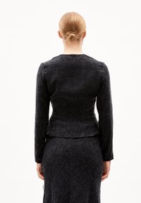 Giacca nera a maniche lunghe con tessuto strutturato, design aderente e orlo svasato. Vista posteriore che mostra una silhouette liscia e ben definita.
