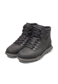 Botas de senderismo de cuero negro con un diseño de tobillo alto, punta redonda y superficie texturizada. Presentan ojales de metal y suela de goma rugosa.