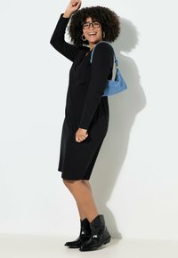 Zwarte jurk met lange mouwen en een losse pasvorm, gecombineerd met een glinsterende blauwe handtas en zwarte cowboylaarzen met zilveren studs.