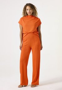 Oranje tweedelige outfit met een hoogsluitend top met korte mouwen en wijde broek met verticale naden. Glad, lichtgewicht stof.