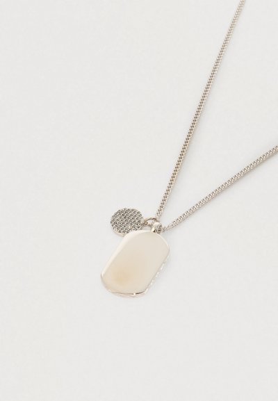 Náhrdelník se zlatavým tónem s hladkým obdélníkovým přívěskem a menším kulatým přívěskem s texturou na jemném řetízku na bílém pozadí.