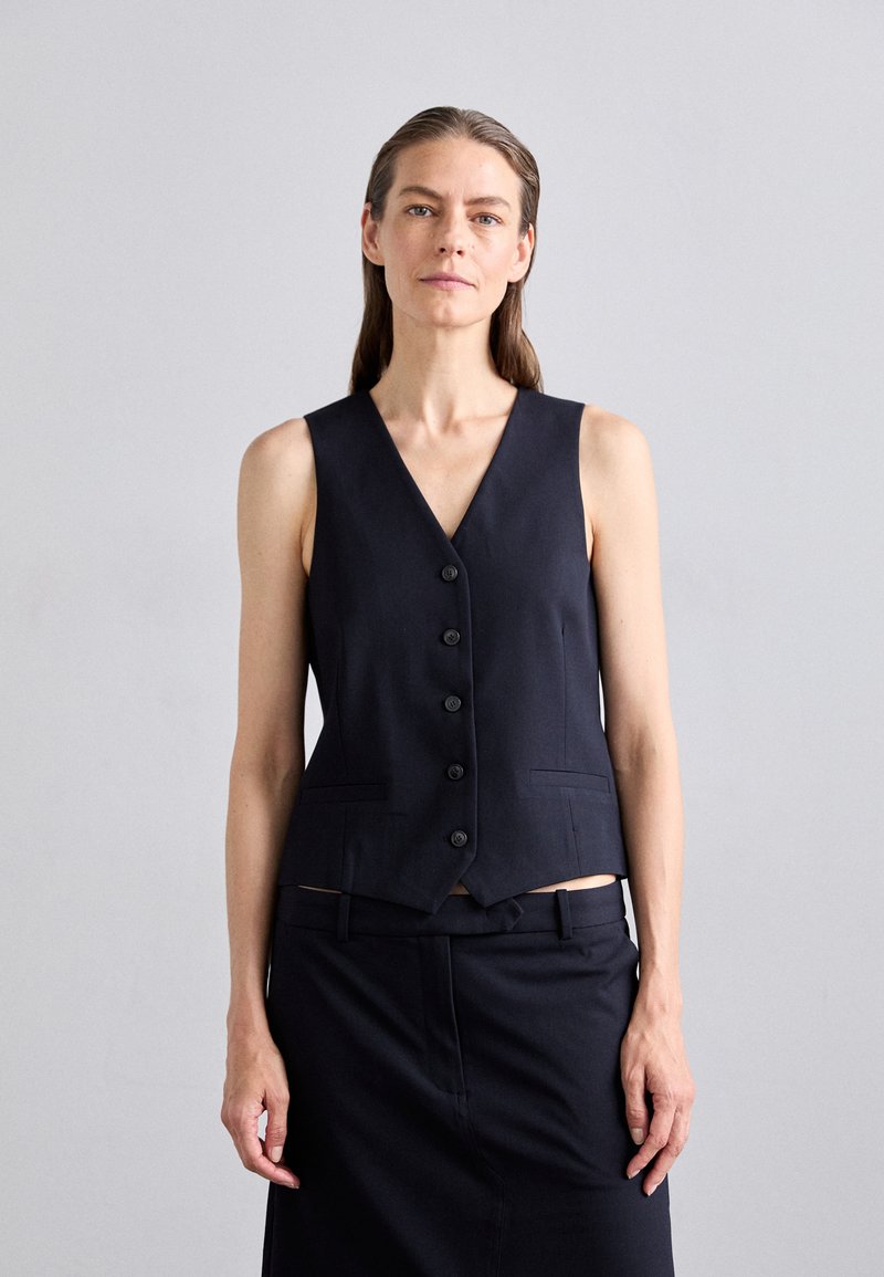 Navy sleeveless vest with a V-neck, five black buttons, and two front pockets. Tailored, structured fit with a smooth texture.