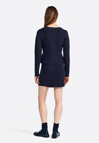 Top de punto azul marino con mangas largas, combinado con una falda ajustada a juego. Textura suave, diseño sencillo y detalle discreto en la parte posterior.