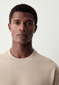 Beige sweatshirts met een ronde hals en geribbelde kraag. Glad oppervlak en aansluitend ontwerp, met een neutraal kleurenpalet.