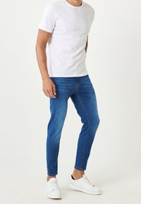 T-shirt bianco in cotone, jeans in denim blu con un design aderente e sneakers bianche. Tessuto liscio con gamba affusolata e nessun motivo visibile.