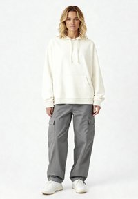 Felpa crema con tasca frontale, abbinata a pantaloni cargo grigi di taglio morbido con tasche laterali. Indossati con sneakers bianche.