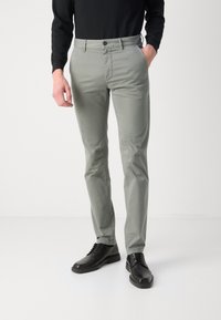 Světle šedé slim-fit kalhoty se prošíváním, předními kapsami a uzávěrem na jeden knoflík, spárované s černými šněrovacími botami.