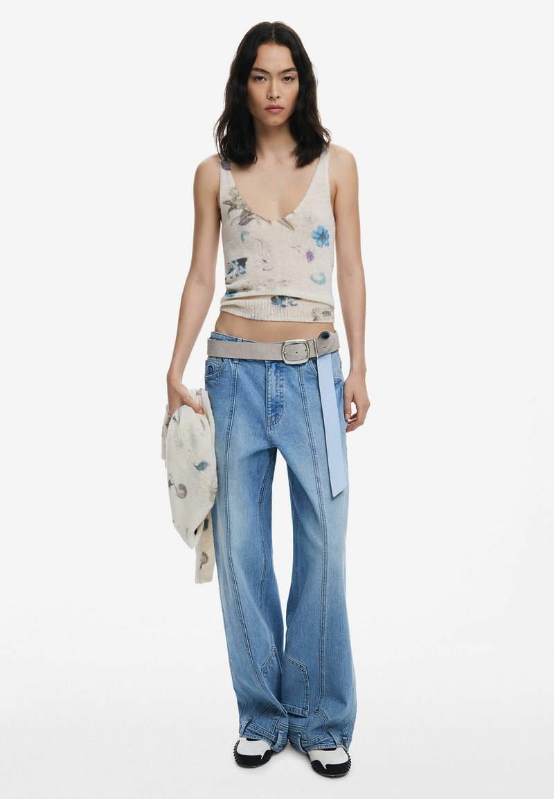 Strick-Tanktop in Creme mit floralem Muster, kombiniert mit hellblauen, weiten Jeans und einem grauen Gürtel. Lässiger Look, ergänzt durch eine Strickjacke.