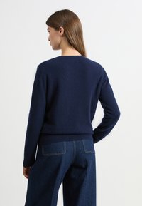 Granatowy, dzianinowy sweter z okrągłym dekoltem, ściągaczami na rękawach i u dołu, o gładkiej fakturze, w zestawieniu z dżinsowymi spodniami.