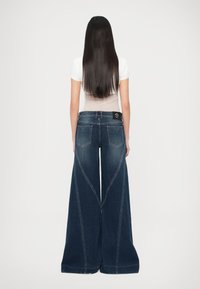 Tmavomodré rifle s voľnými nohavicami a vysokým pásom, s výraznými trojuholníkovými švami a dvoma zadnými vreckami.