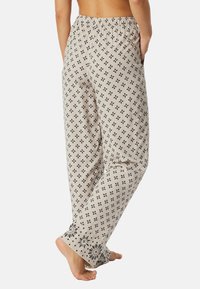 Lichte, beige geprinte broek met een wijde pijp, voorzien van een zwart geometrisch ontwerp en een elastische tailleband. Inclusief zijzakken.