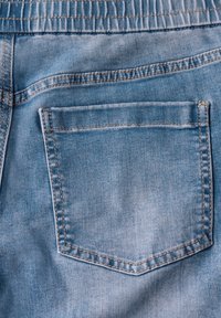 Jeans de mezclilla azul claro que presentan un bolsillo trasero central de forma rectangular, detalles de costura visibles y una textura ligeramente desgastada.