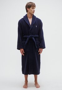 Marineblå badekåpe laget av mykt materiale, med lange ermer, belte, to fremre lommer og en liten logo på brystet.