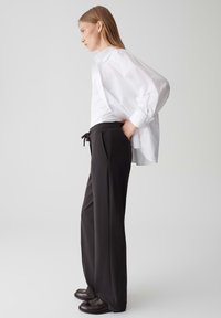 Pantaloni neri a gamba larga con vita con cordino, abbinati a una camicia bianca oversize con bottoni. Tessuto liscio e design minimalista.