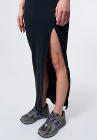 Abito a coste nere con spacco laterale, abbinato a scarpe da ginnastica grey New Balance. Il tessuto dell'abito è strutturato; le scarpe presentano dettagli in mesh.