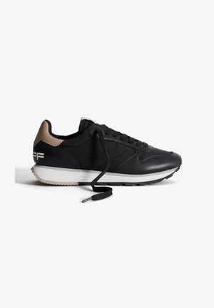 Scarpa sportiva nera con tomaia in pelle liscia, tallone beige a contrasto, punta rotonda, lacci neri e suola in gomma bianca con battistrada testurizzato.