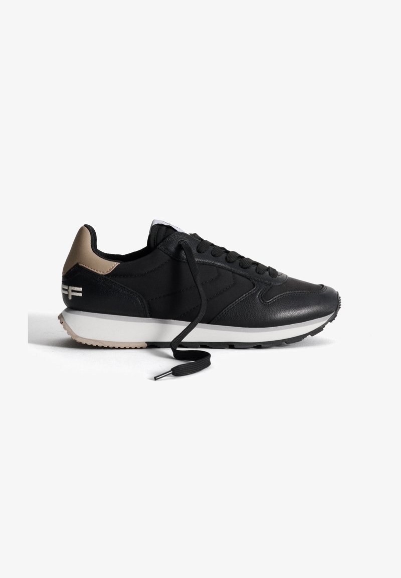 Scarpa sportiva nera con tomaia in pelle liscia, tallone beige a contrasto, punta rotonda, lacci neri e suola in gomma bianca con battistrada testurizzato.