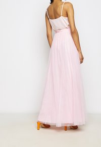 Lång rosa tyllkjol med ett genomskinligt material, parat med en satinblus och orange högklackade skor. Har en bälte i midjan som detalj.