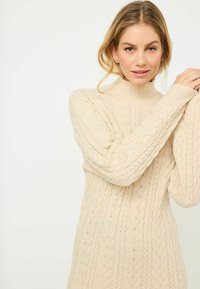Maglione beige a maglia con colletto alto, caratterizzato da un motivo a trecce e polsini a costine. Morbida texture, vestibilità casual oversize.