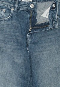 Jeans in denim blu scuro con chiusura a zip e bottone. Presentano un taschino frontale e una texture leggermente consumata.