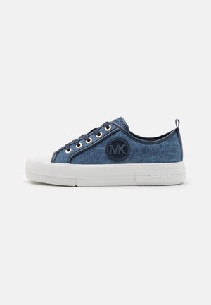 Lavskrids blå denim sneaker med hvid tyk sål, sorte snørebånd, rundt MK-logo på siden og trækstrop ved hælen.