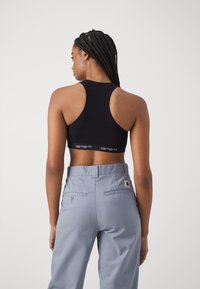 Black racerback sports bra with "Carhartt" logo on the band, paired with light blue pants featuring back pockets and a logo patch.