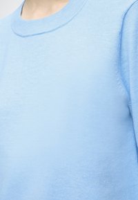 Jasnoniebieski sweter typu pullover wykonany z miękkiej dzianiny. Posiada okrągły dekolt i gładką fakturę, z widocznym przeszyciem na szwach.