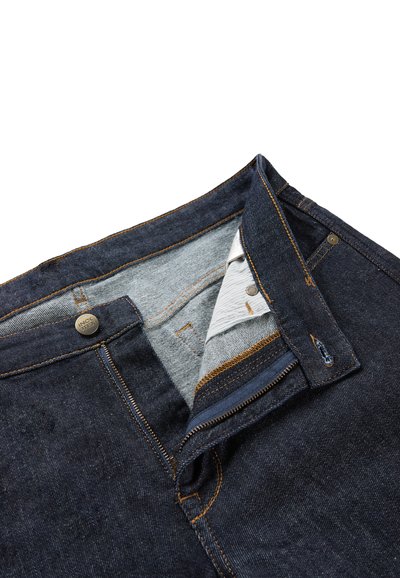 Jean en denim bleu foncé avec braguette zippée, surpiqûres orange et doublure en tissu gris à l'intérieur de la taille. Bouton en métal marqué au niveau de la fermeture.