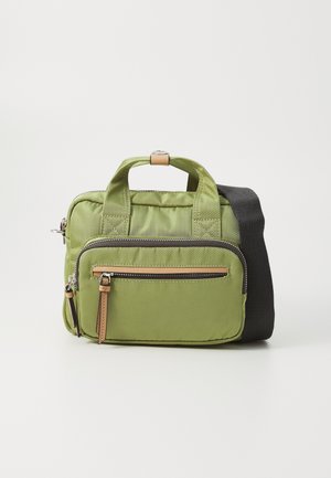 Sac bandoulière en tissu vert avec poche zippée à l'avant, doubles poignées et large bandoulière noire réglable sur fond uni.
