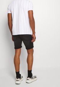 T-shirt bianco a righe con maniche corte, abbinato a pantaloncini di jeans neri con risvolti visibili, calze nere e sneakers bianche.
