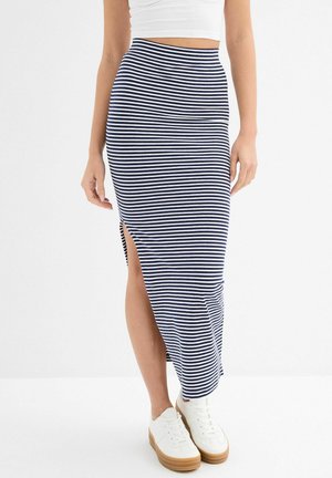 Mujer con falda midi de rayas azul marino y blancas con una abertura lateral, top corto blanco y zapatillas blancas con suelas de goma.