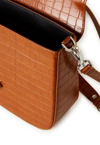 Brązowa torba ze skóry tłoczonej w wzór krokodyla, o teksturowanej powierzchni, z magnetycznym zapięciem na klapę i srebrnym metalowym zapięciem. Wnętrze jest czarne.