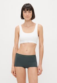Bralette branca com decote arredondado e textura suave, acompanhada de calções de boyshorts verde-esmeralda com uma cintura elástica. Design simples e funcional.