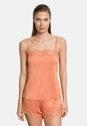 Mujer con camisola sin mangas de satén color melocotón y shorts a juego con encaje en los bordes, sobre un fondo liso y claro.