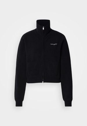 Čierna mikina na zips s vysokým golierom, dvoma prednými vreckami a rebrovanými manžetami. Na hrudi je malá biela logo. Mäkká textúra.