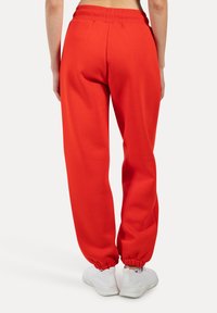 Rode sweatpants van zachte stof met een relaxte pasvorm, elastische tailleband en gathered cuffs. Draagt witte sneakers.