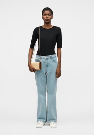 Naine, kes kannab musta küünarnukipikendusega topi, hele siniseid laia säärega pükse, valgeid tossusid ja beeži rinna äärde riputatud kotti kuldse kettpaelaga.