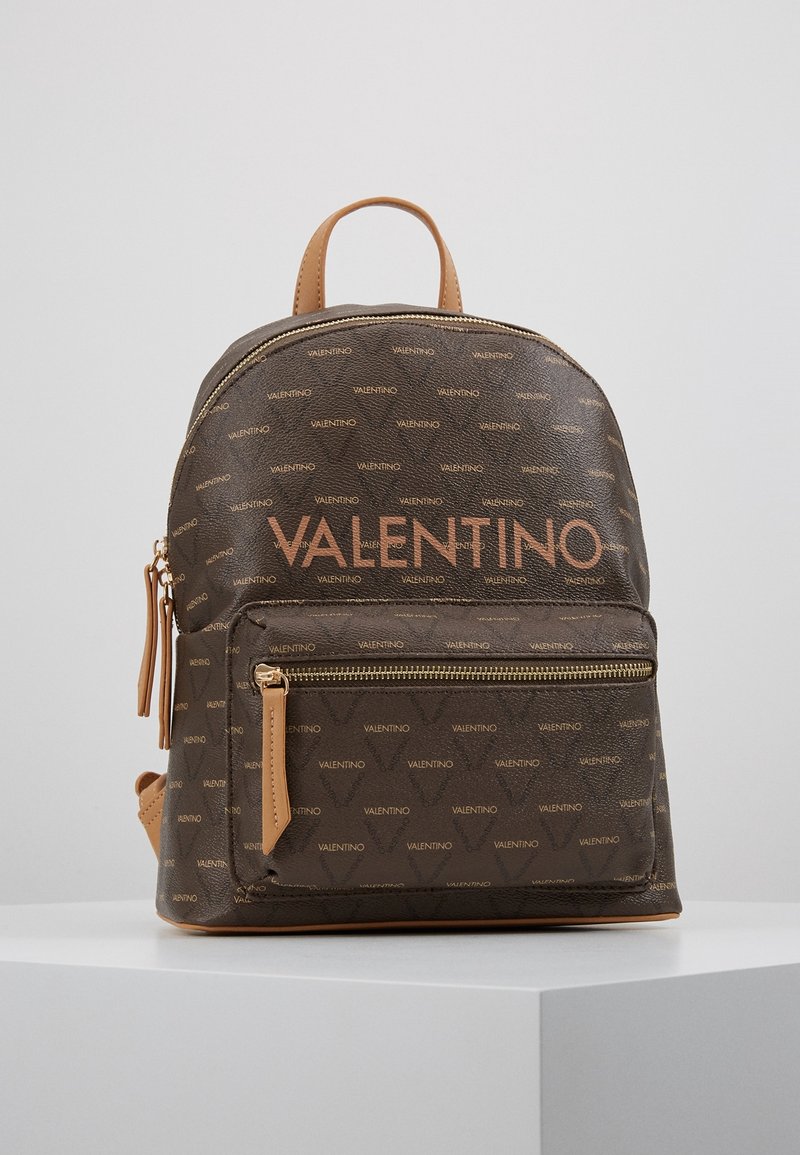 Ruskea kuvioitu reppu, jossa on brändinimi "VALENTINO" oranssilla. Varustettu vetoketjullisella etutaskulla ja vaaleanruskeilla yksityiskohdilla olkahihnoissa.